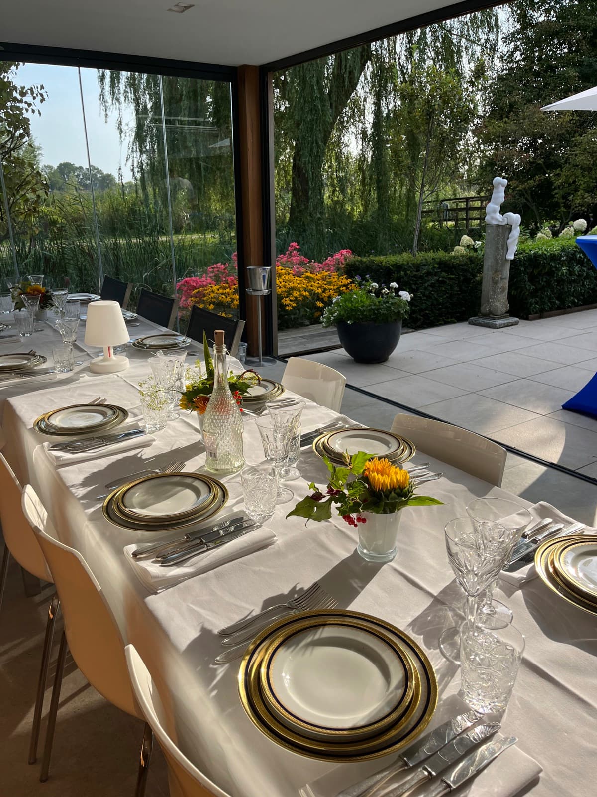 Gedekte tafel in een serre met uitzicht op de tuin, gouden borden en zonnebloemen