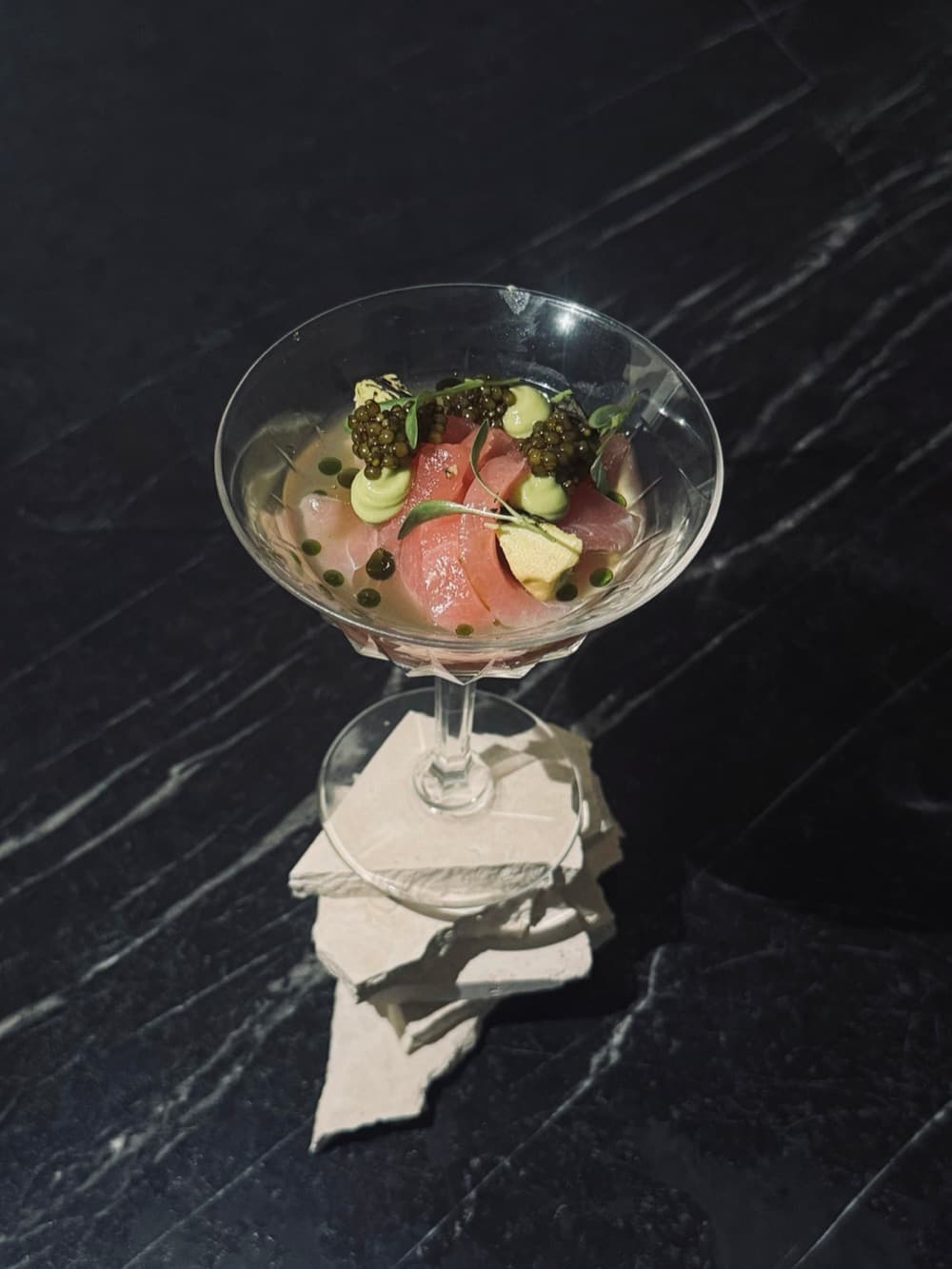 Coupe met tartaar, komkommer en kaviaar op zwart marmer, met een linnen servet