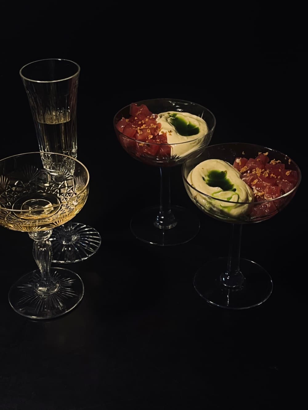 Drie coupes met tartaar en avocado naast glazen champagne op een donkere ondergrond